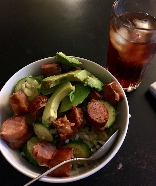 Zucchini cauliflower rice stir fry with red peppers, onions, and garlic with sausage and sliced avocado on top.